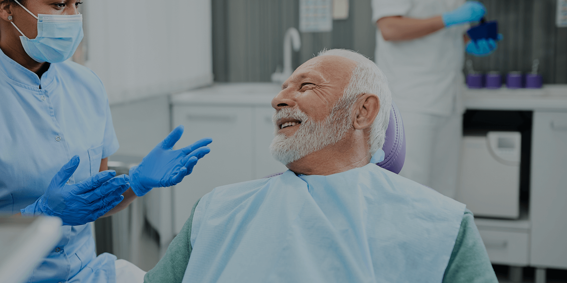 Older man seated in dental chair looking at dentist.
