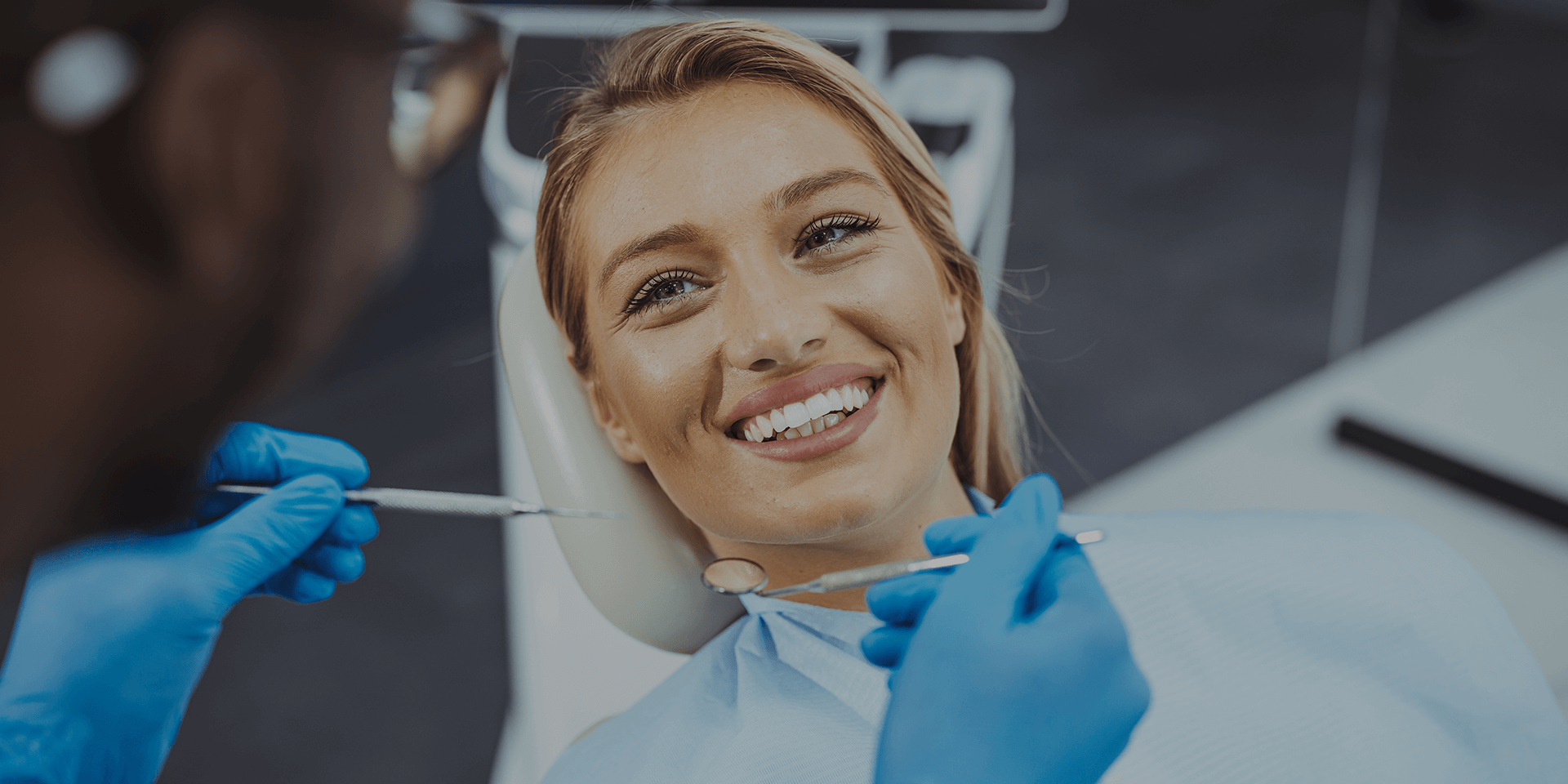 A woman smiling with dentist holding dental tools near her face.