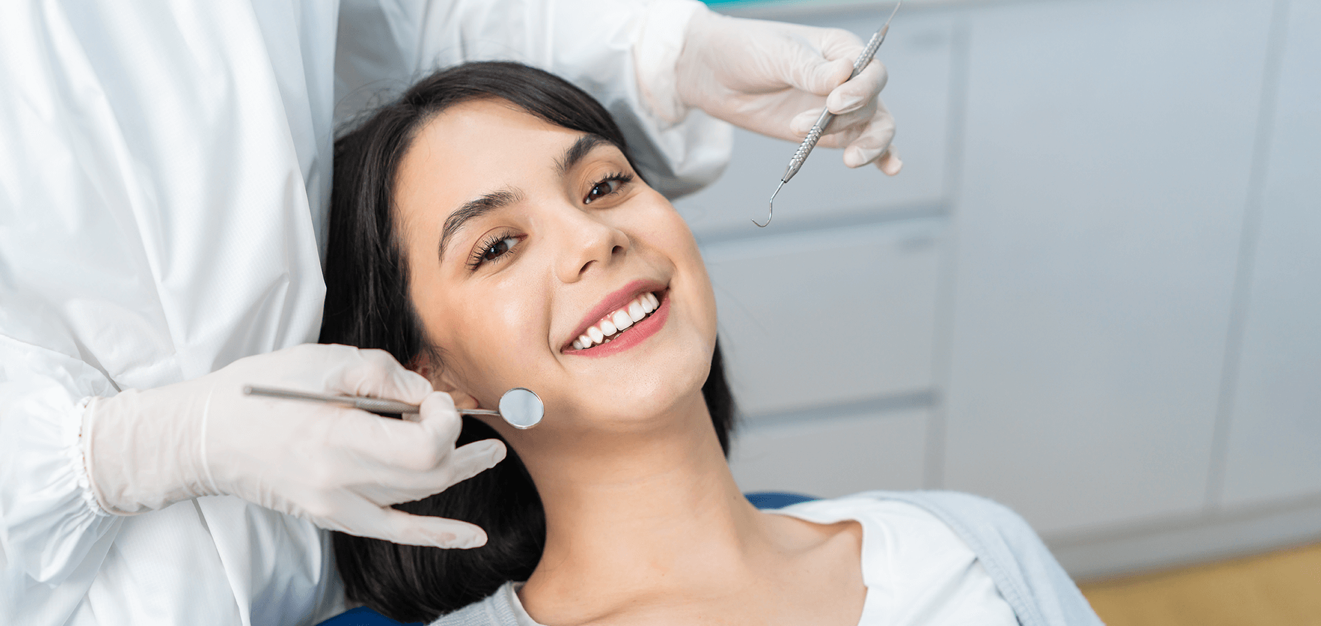 A woman smiling with dentist holding dental tools near her face.