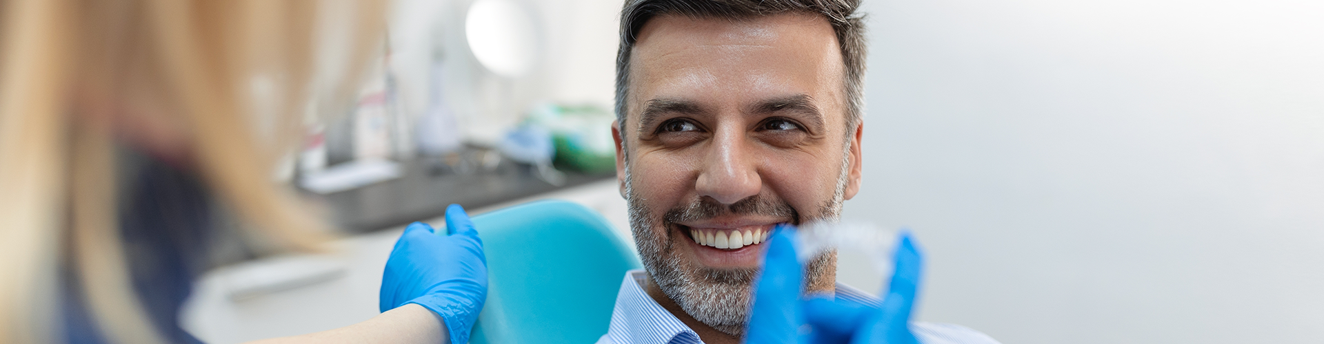 gloved hands holding clear aligner in front of smiling man